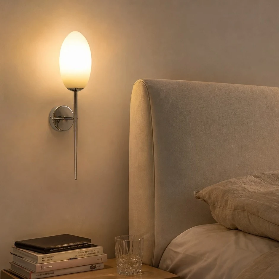 Milk glass wall sconce beside an upholstered bed